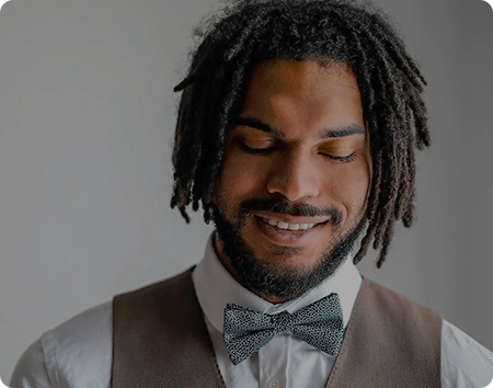 A man with dreadlocks wearing a vest and bow tie.