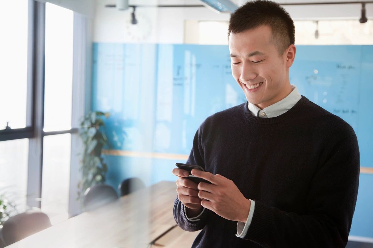 A man is smiling while looking at his phone.