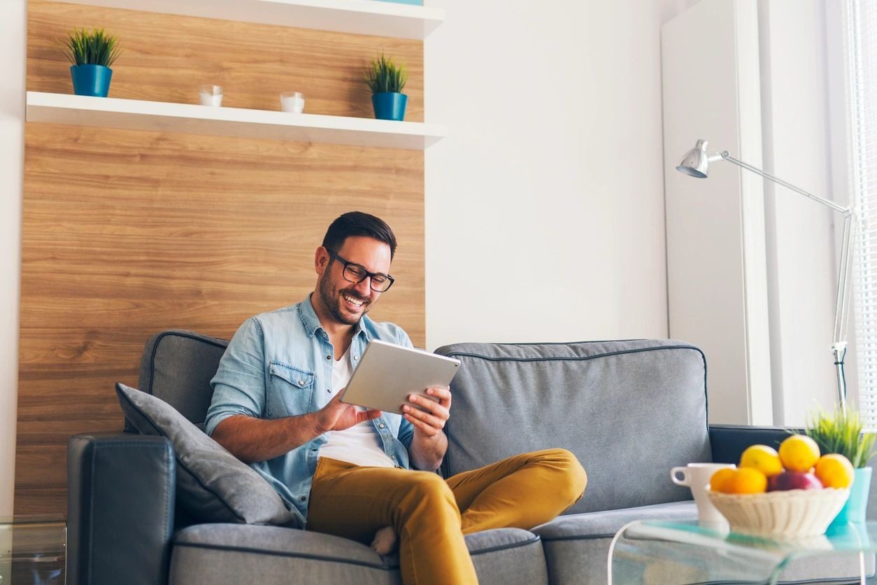 A man sitting on top of a couch holding an ipad.